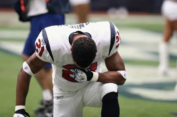 An NFL player in uniform takes a knee.