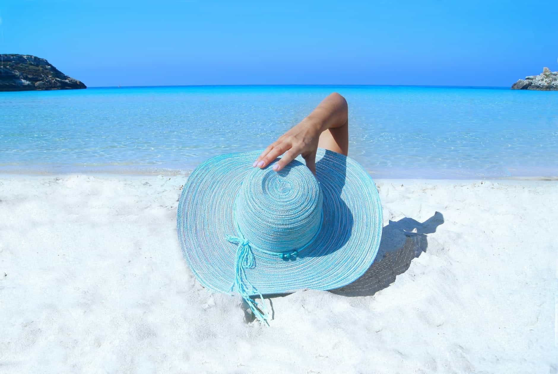 A woman lying on a beach with a blue hat.