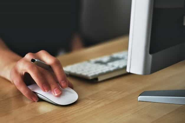 A person holding a computer mouse, working with a monitor and keyboard.