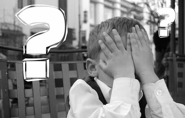 A young boy holding his hands to his face with large question marks floating around him.