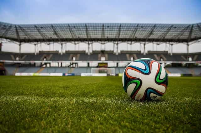 A football on a grass pitch in a stadium.