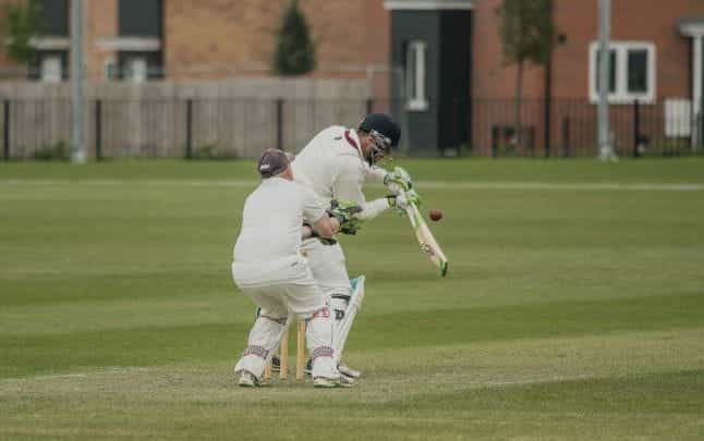 Man in white clothing hits a cricket ball with a bat.