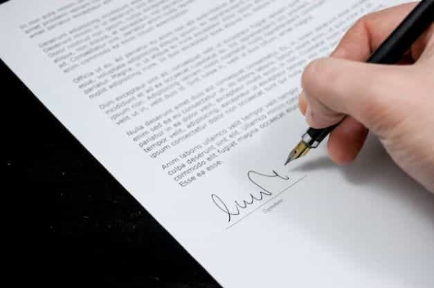 A hand signing a letter with a pen.