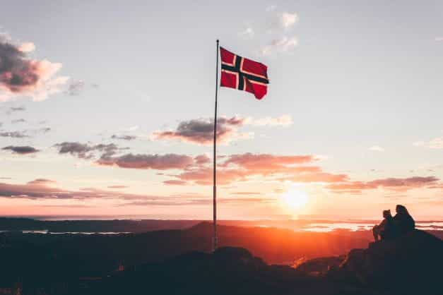 A Norway flag on a flagpole at dusk.