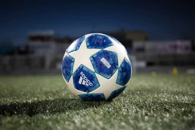 A static blue and white UEFA league branded Adidas football on the turf, under floodlights.