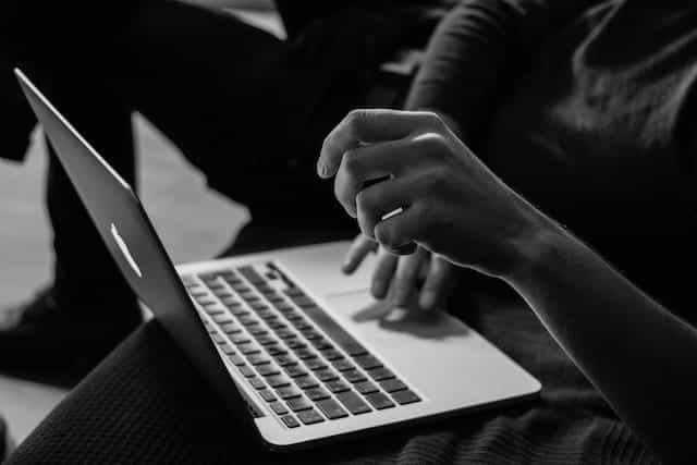 A laptop balances on someone’s knee as they use the keyboard.