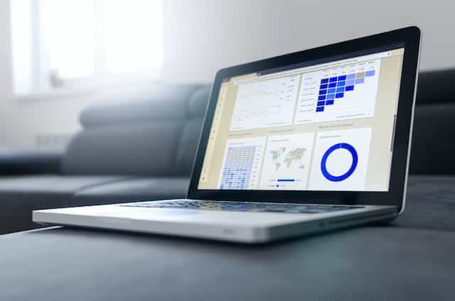 An open laptop displays a report document with various graphs and charts.