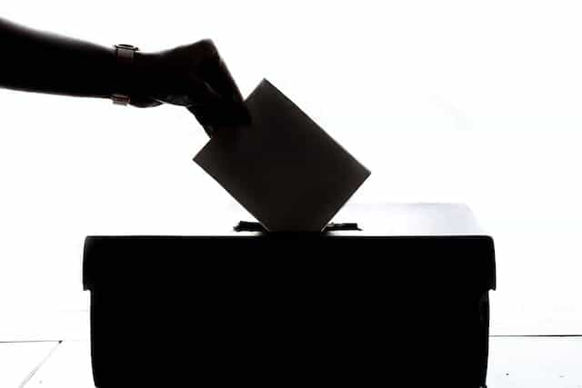 A silhouetted hand posts a vote into a ballot box.