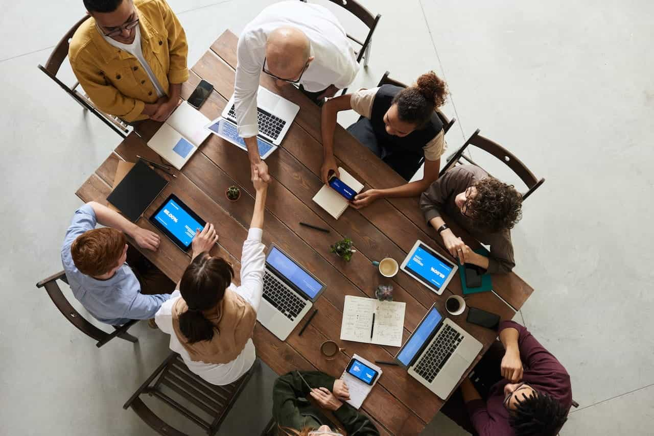 Colleagues sit around a table in a meeting with laptops.