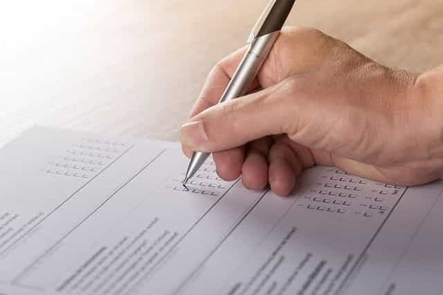 A person’s hand filling out a multiple choice survey on a form on a piece of paper.