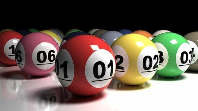 A collection of different colored lottery balls with different numbers on them placed carefully beside one another on a white table surface.