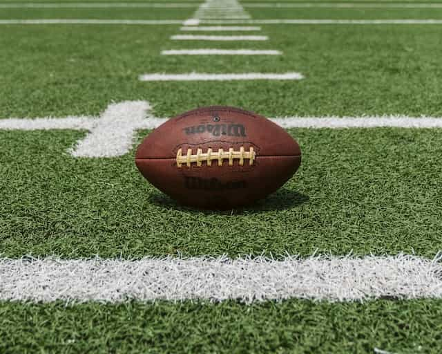 A classic brown American football sitting on a grass pitch at the start of a big game.