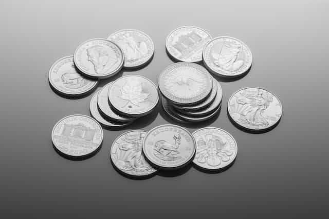 A selection of various silver coins lying flat on a surface, with some facing and showing their heads side, while others face down showing their tails side.