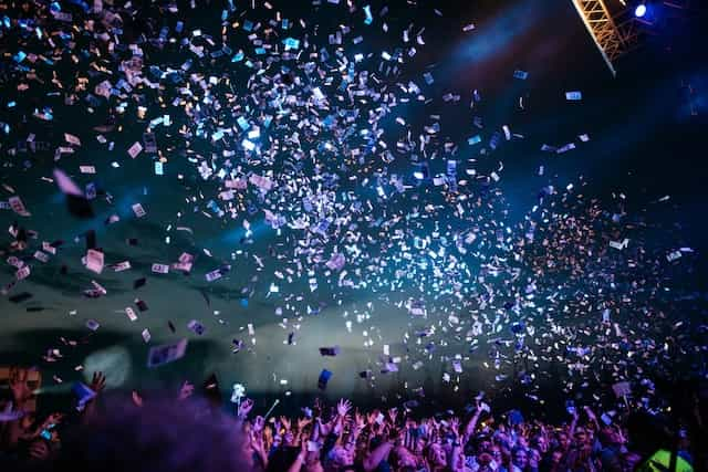 Purple confetti flying across the sky above people partying.