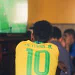 A man wearing a Brazilian soccer jersey watches a game on the television.