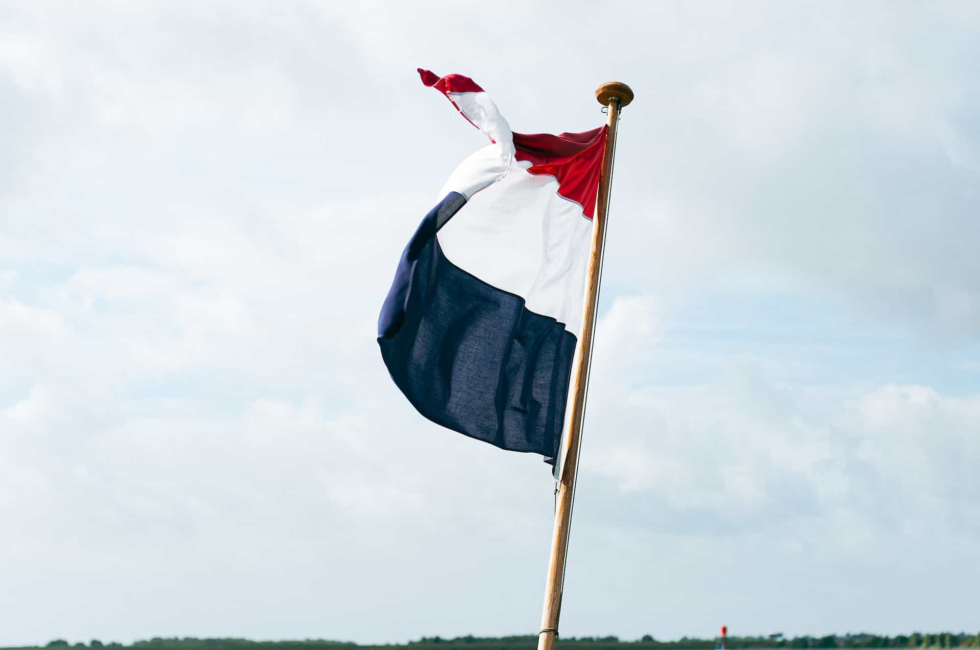 A red, white, and blue flag against a pale blue sky.